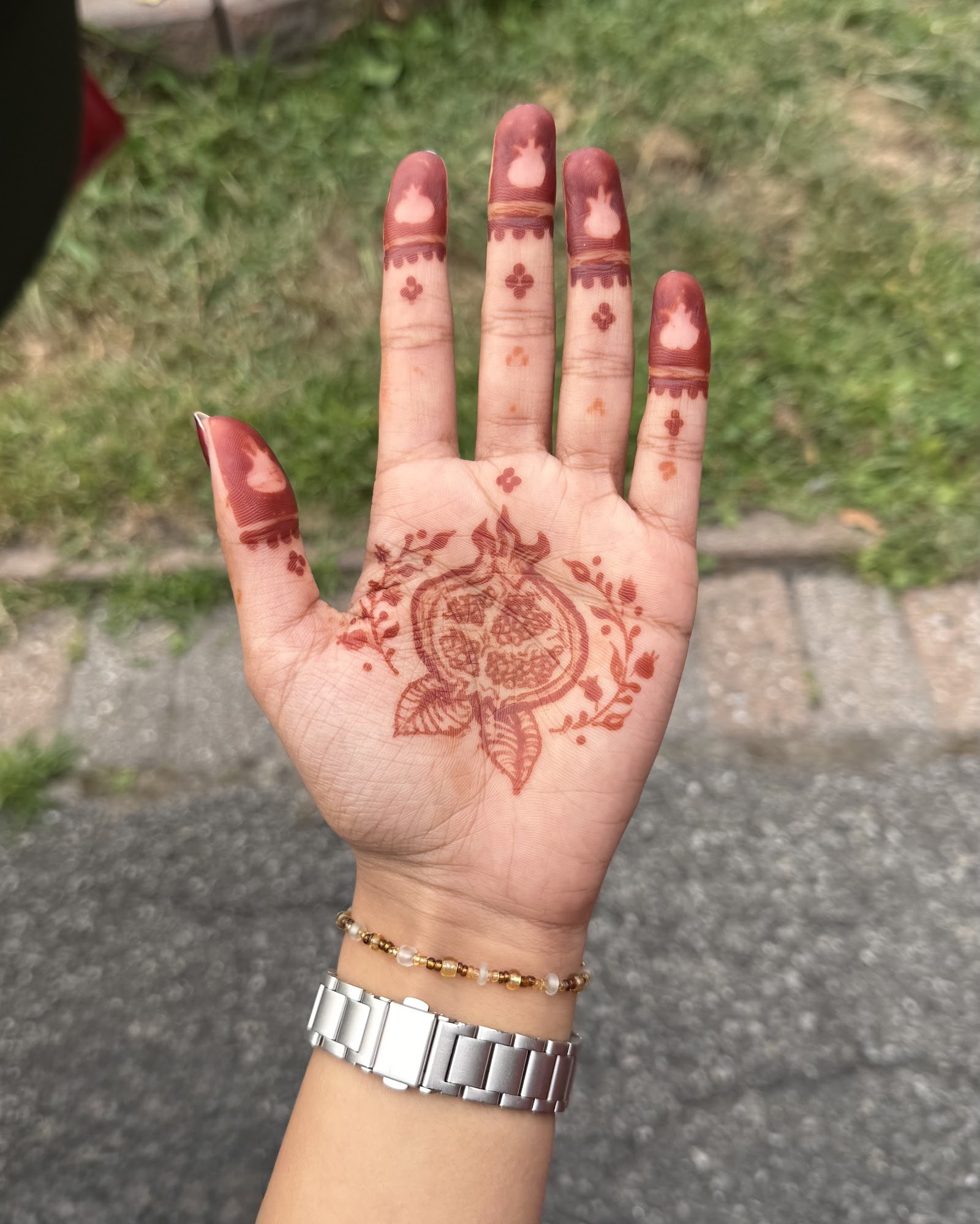A close-up of an ornate NooniDesigns henna design on a hand, showing fine detailed line work.