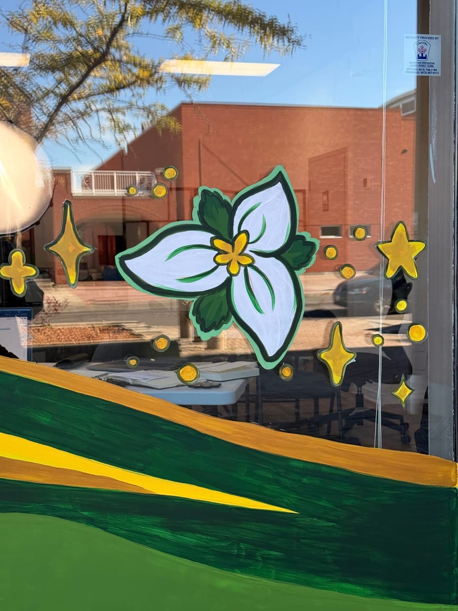 A hand-painted trillium with yellow stars and rolling green and gold hills on an Orléans storefront window.